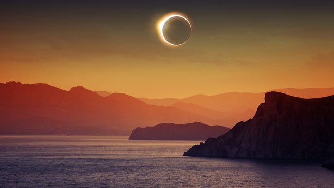 A total solar eclipse over water and mountains