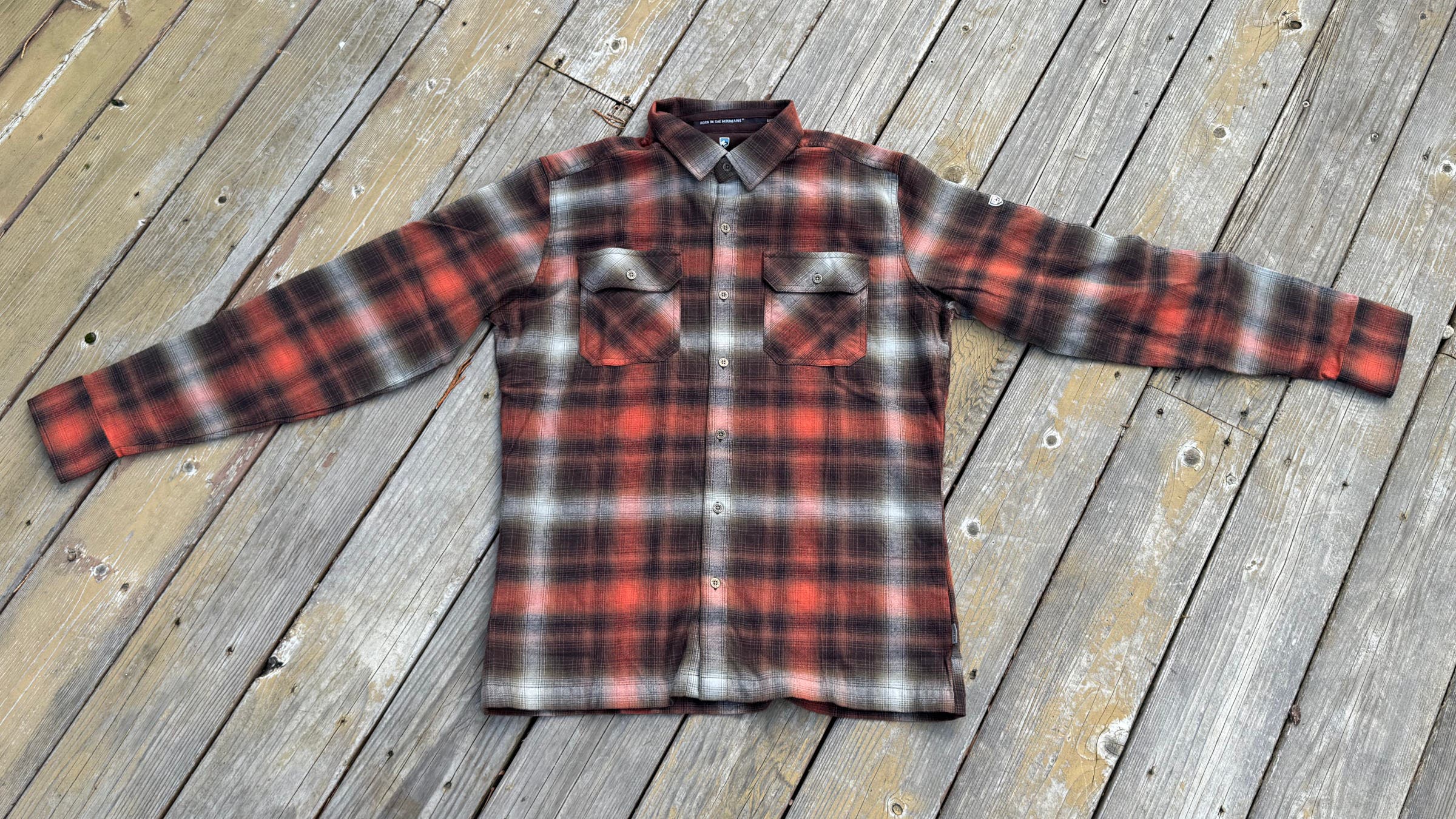 A red, black, and white plaid-patterned Kuhl Dilingr Flannel shirt for men, arranged for display on aged wooden decking