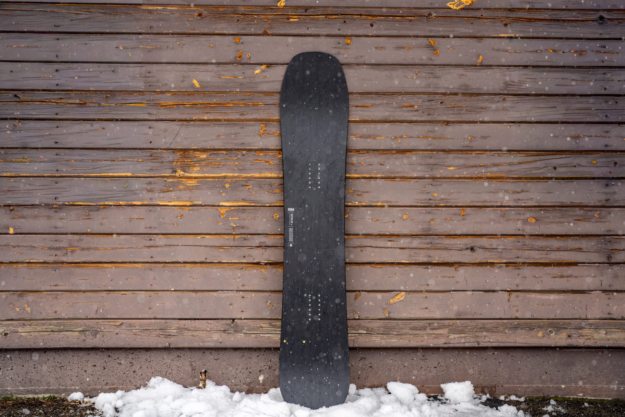 Korua Otto Plus snowboard leans against weathered building