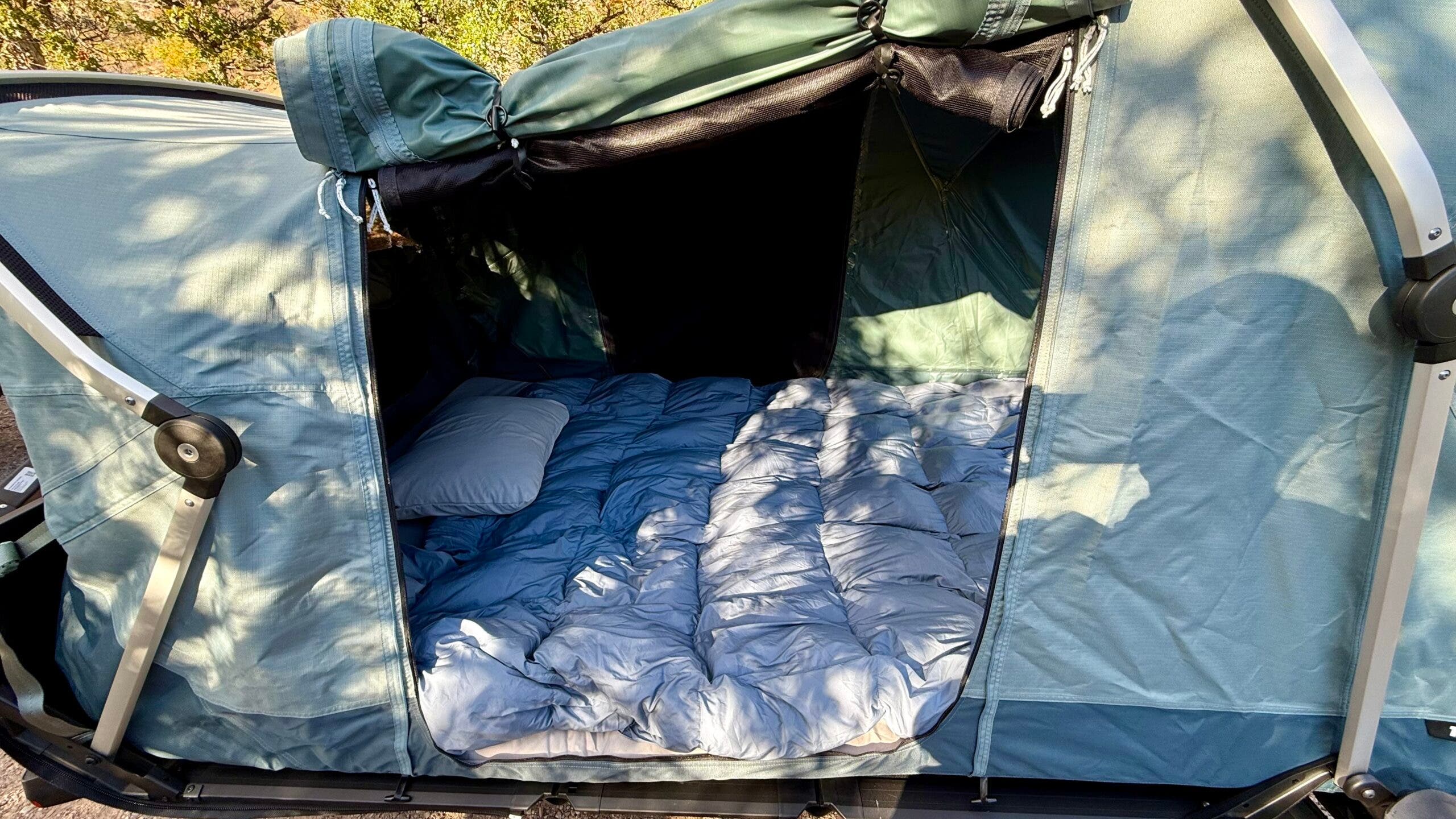 A light blue off-the-ground Thule Outset car camping tent with flap open revealing inside
