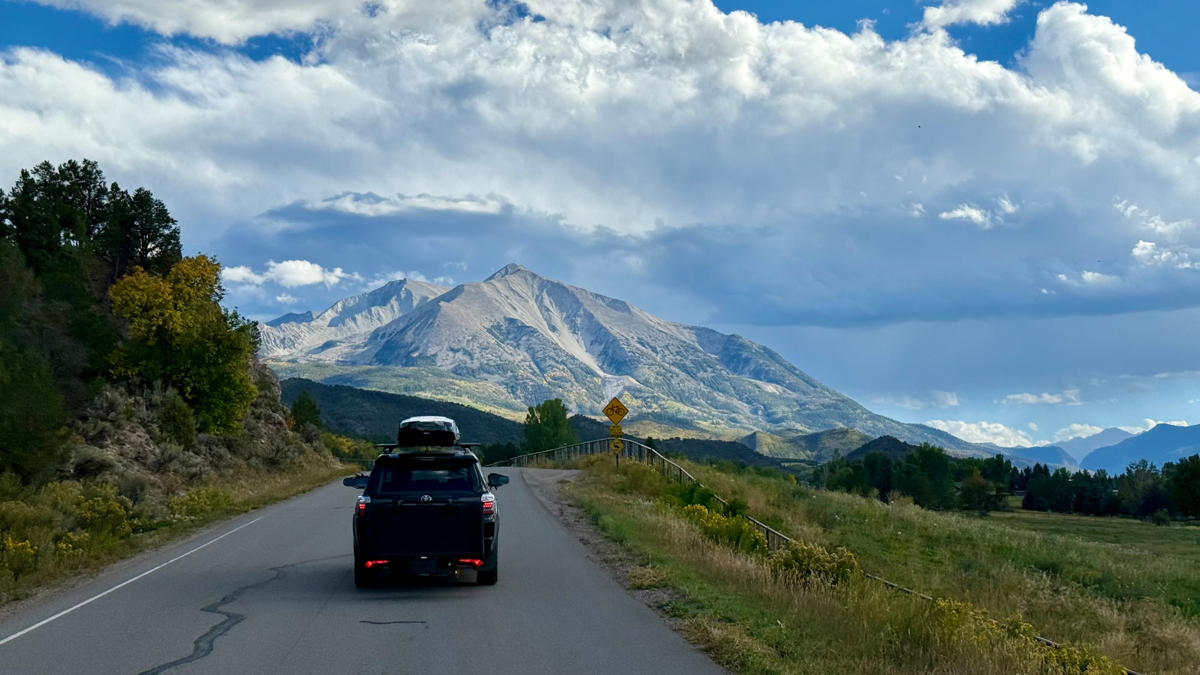 a Toyota 4Runner with folded up Thule Outset in the hitch driving on the road toward the mountains in Colorado