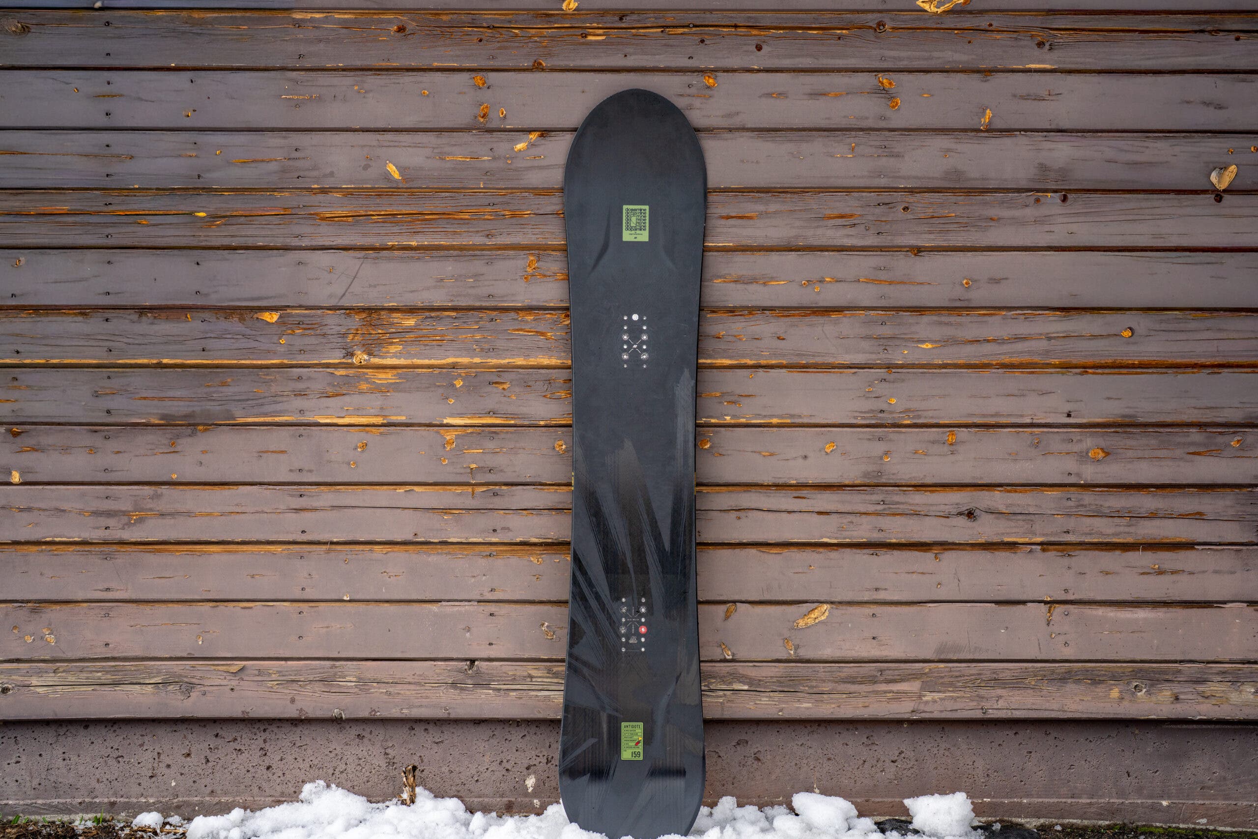 black snowboard K2 Antidote leaning against weathered building