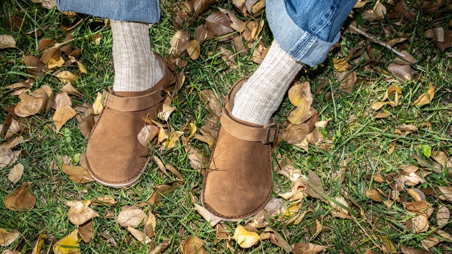men's feet with socks and Birkenstock clogs with jeans and green grass and leaves underneath