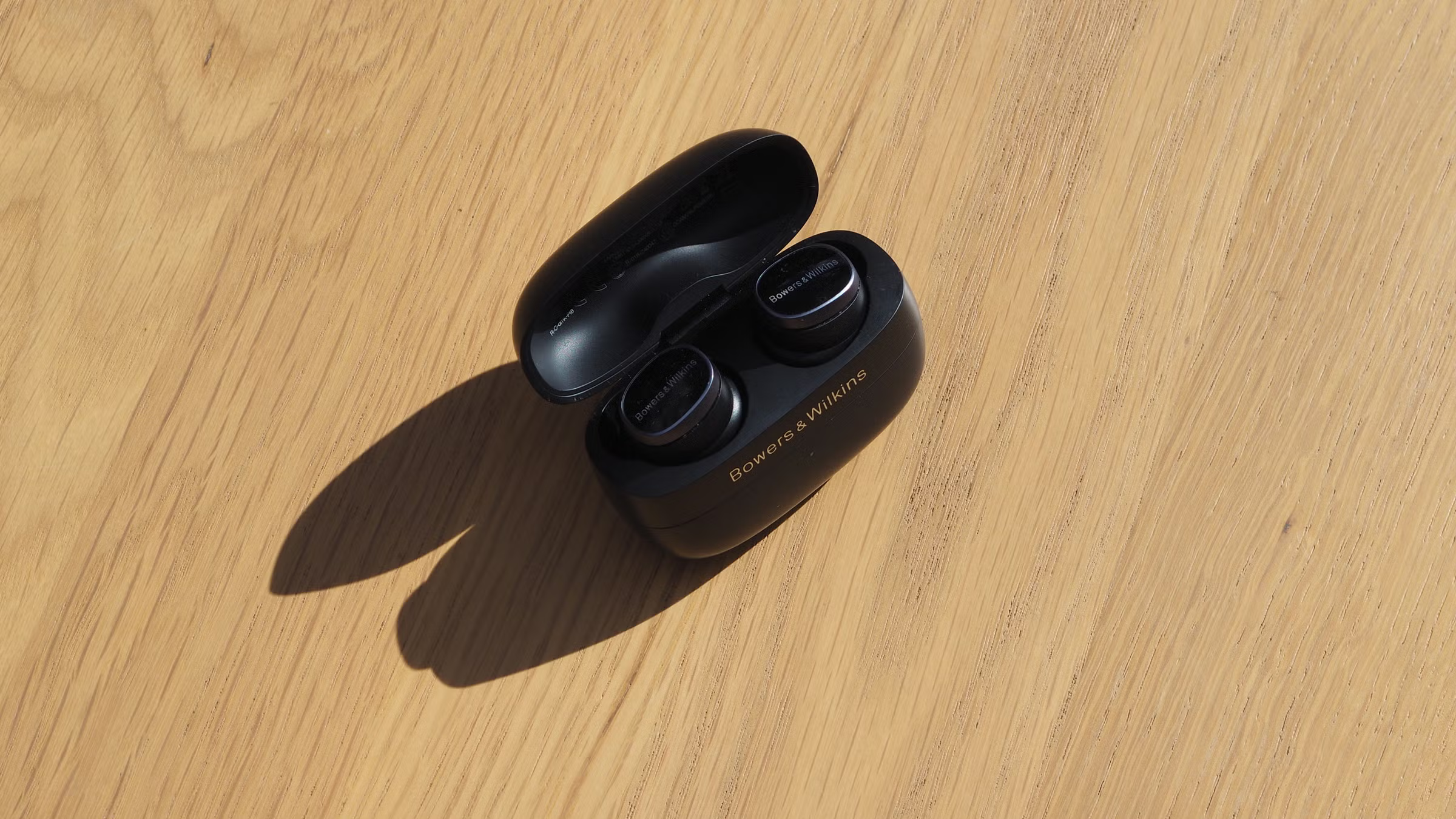 Bowers & Wilkins Pi8 In-Ear True Wireless Earbuds black sport earbuds inside of charging charging case on wooden surface