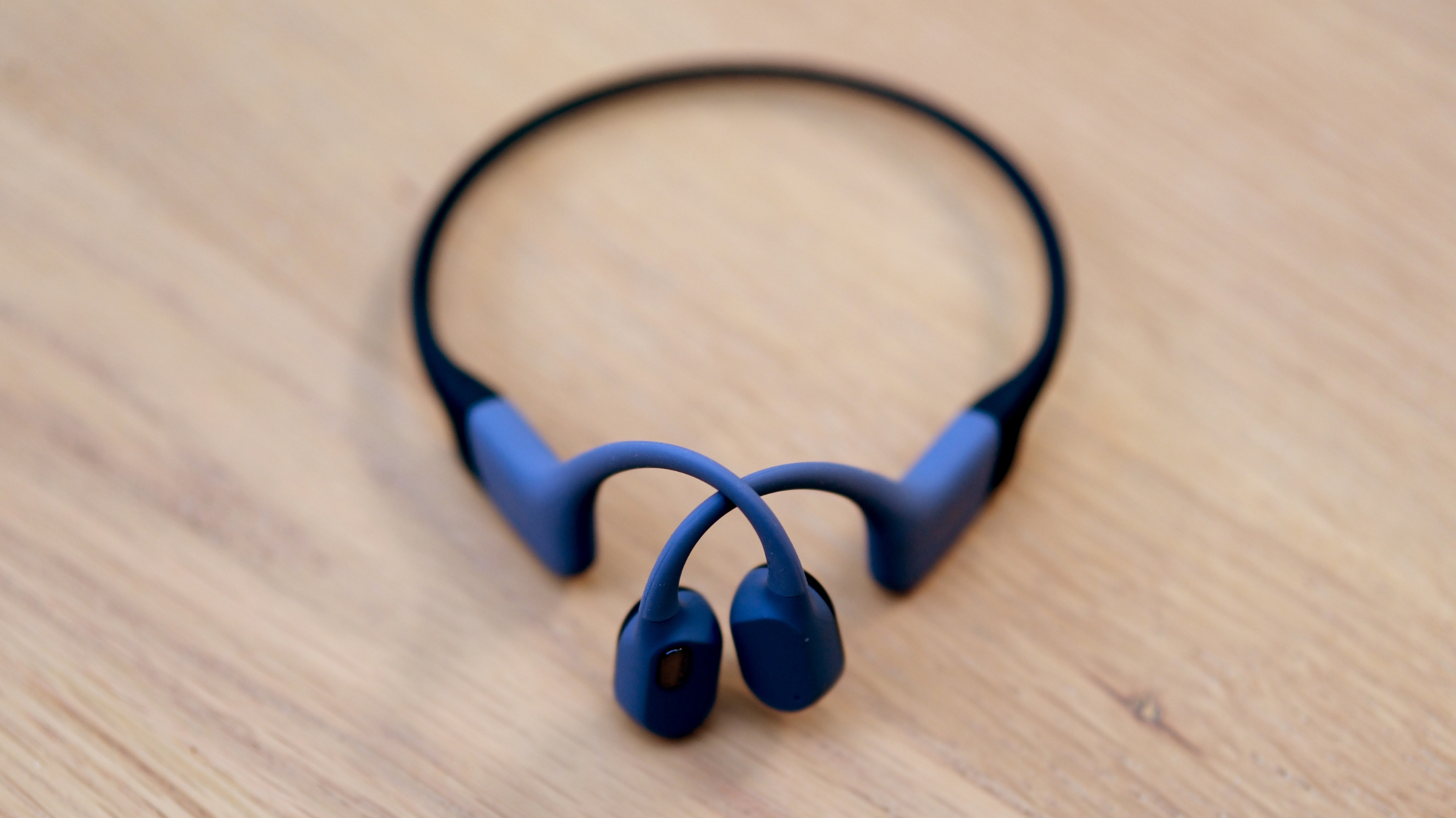 Shokz OpenSwim Pro wrap-around bone-conduction headphones on wooden surface