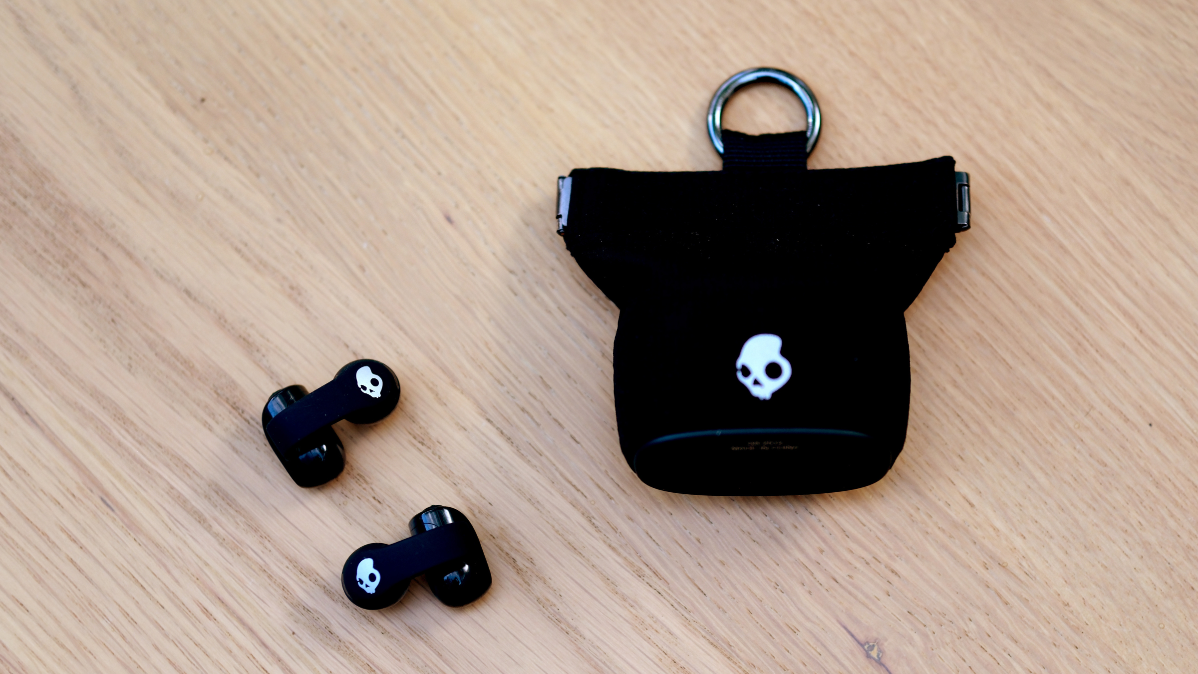 Skull Candy black earbuds next to black case on wood surface as best open-ear earbuds