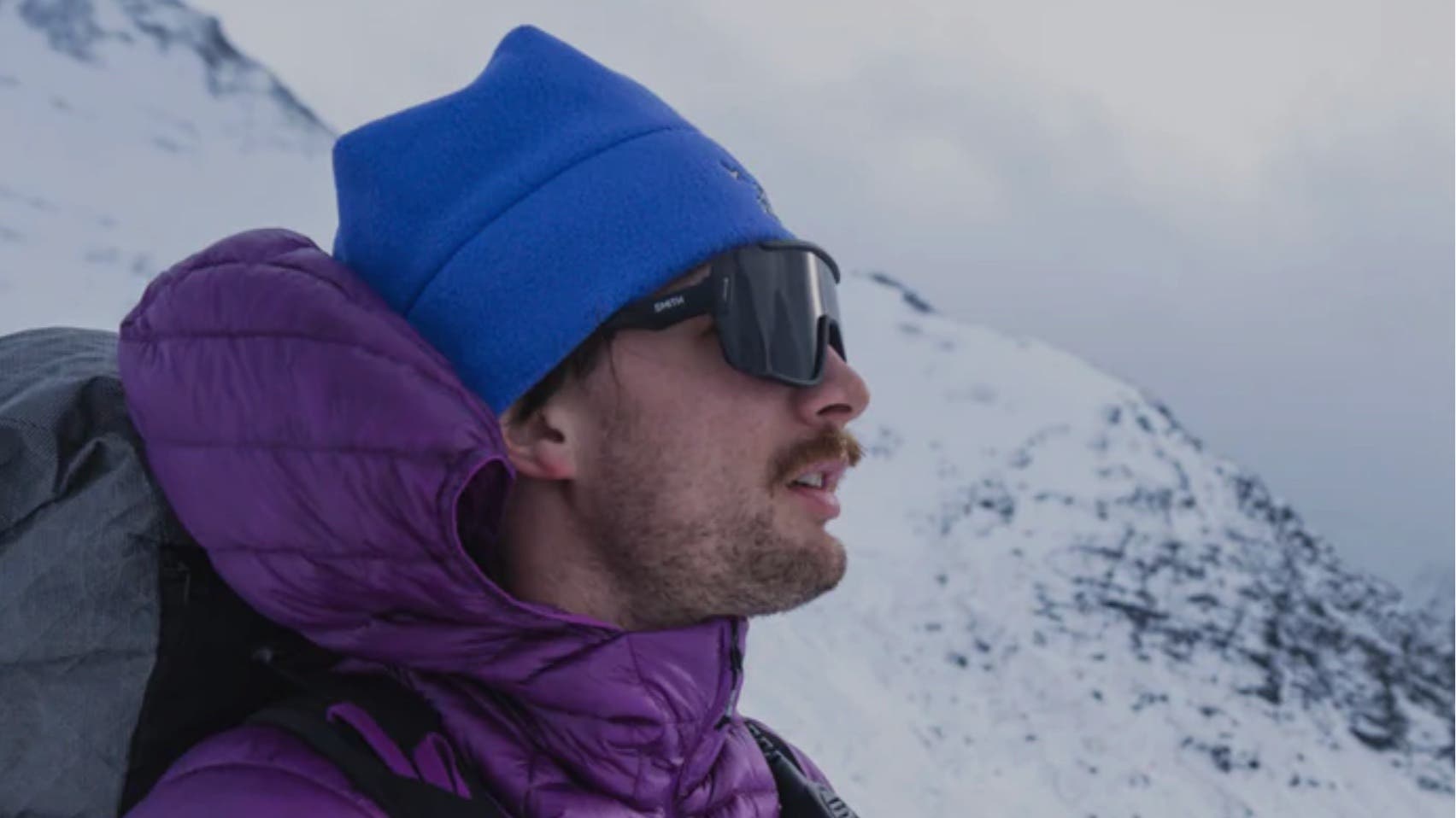 guy wearing purple black diamond jacket and blue hat in the snow