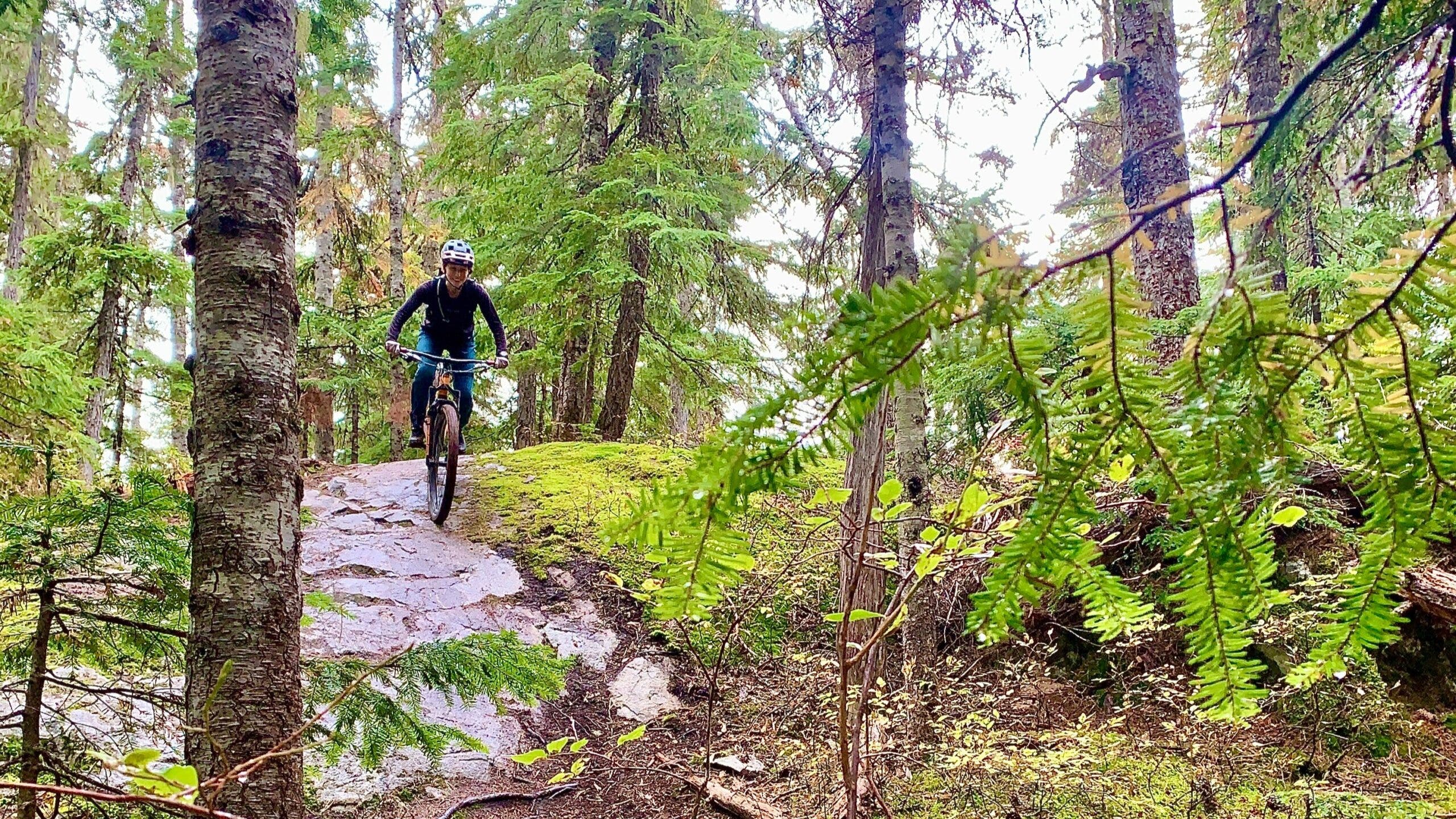 girl riding mountain bike in the woods down a slick rock