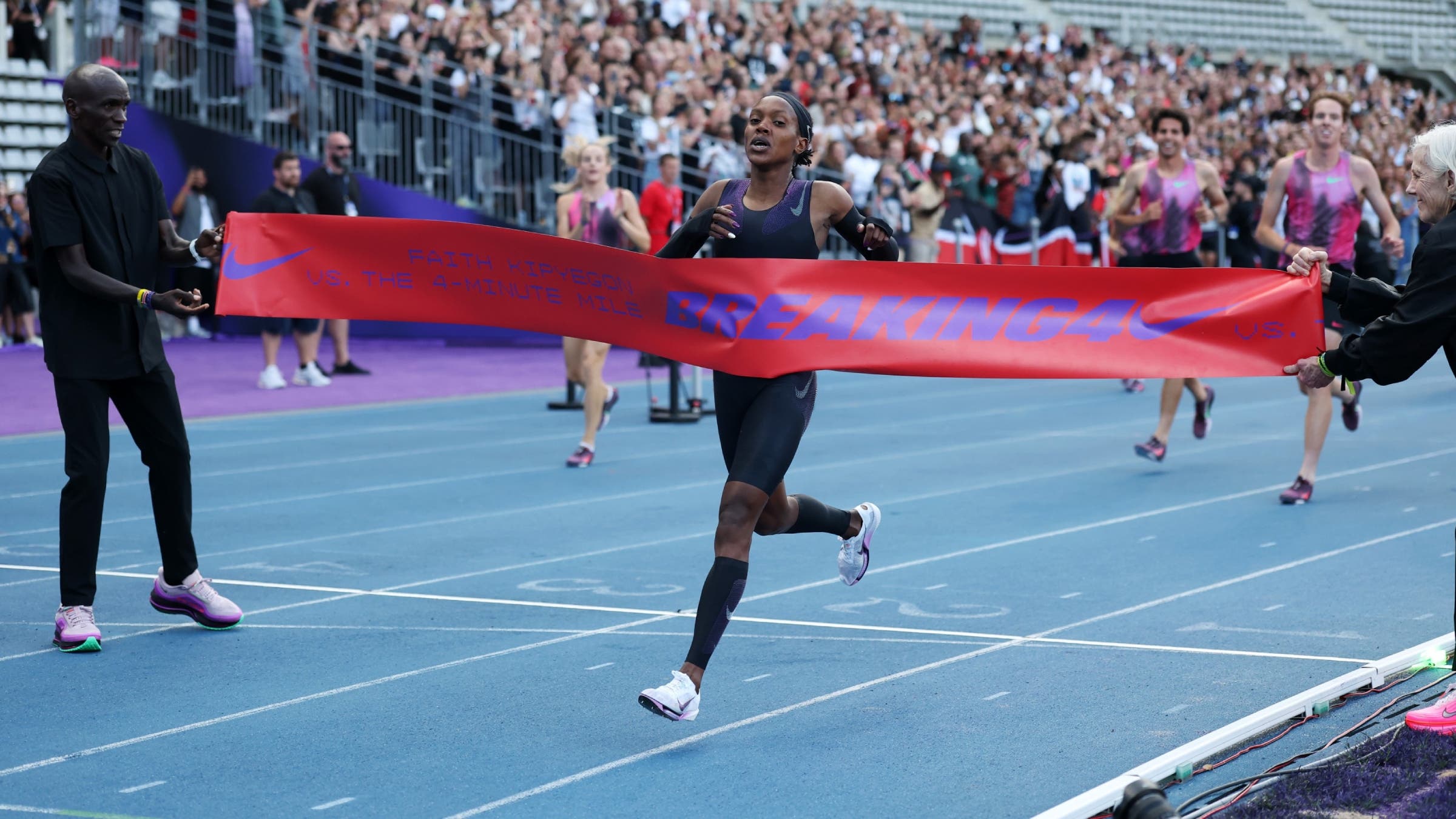 Faith Kipyegon crosses a pink banner on a running track.