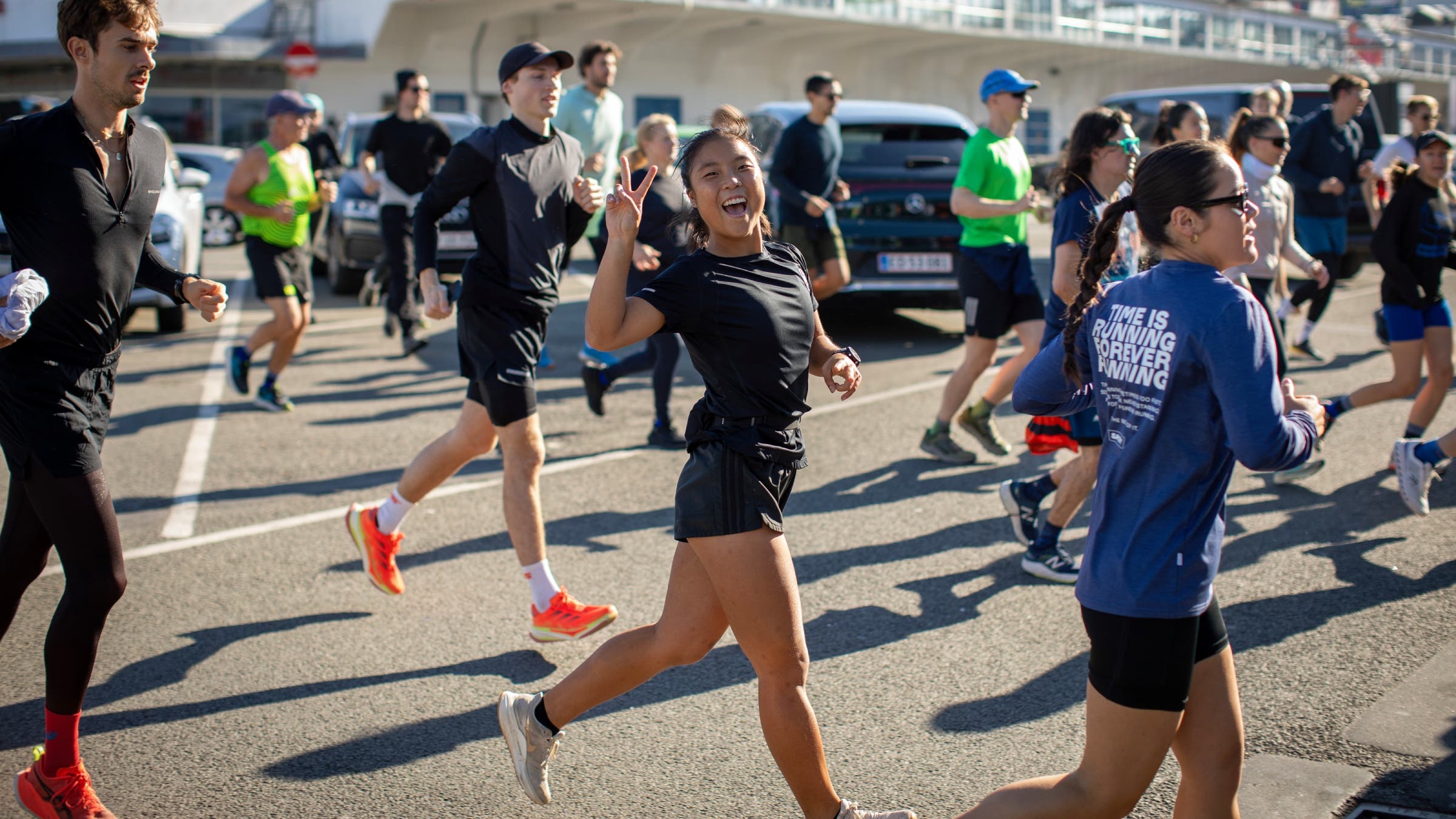 A woman in a crowd of runners gives a peace sign to the camera.