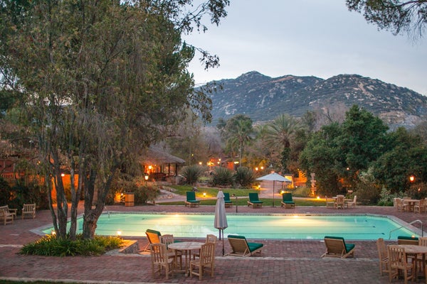 A resort pool at the foot of a mountain during dusk.