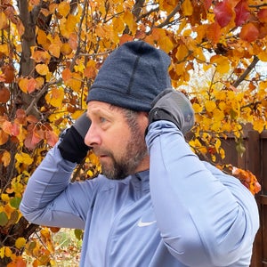man putting on winter running hat and gloves in front of autumnal tree