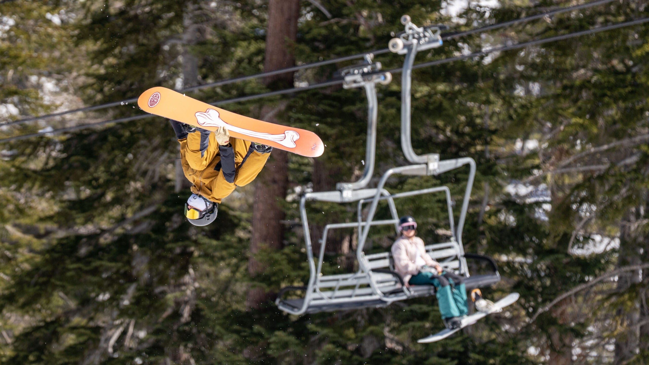 Snowboarder in mid air while people observe from a chairlift