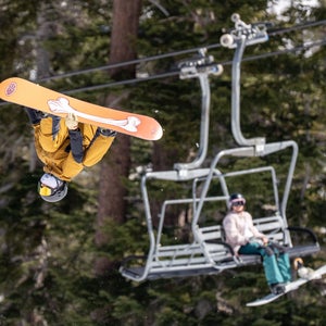 Snowboarder in mid air while people observe from a chairlift