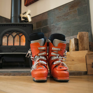 Orange ski boots with custom ski boot liner in front of wood burning stove