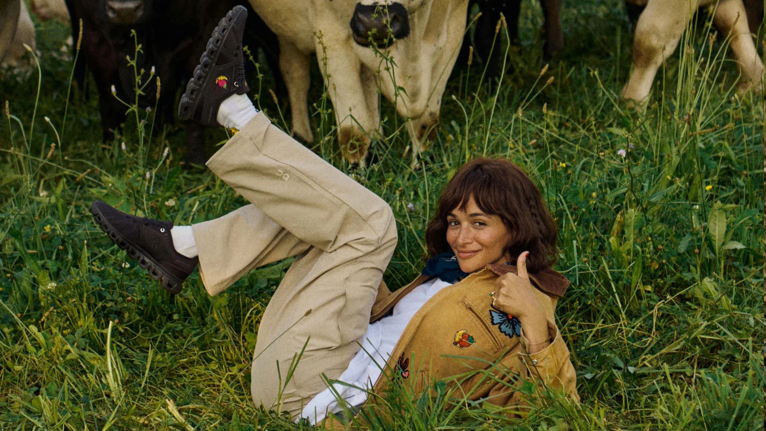 girl wearing workwear in the grass next to a cow
