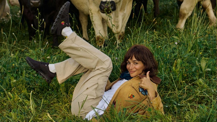 girl wearing workwear in the grass next to a cow