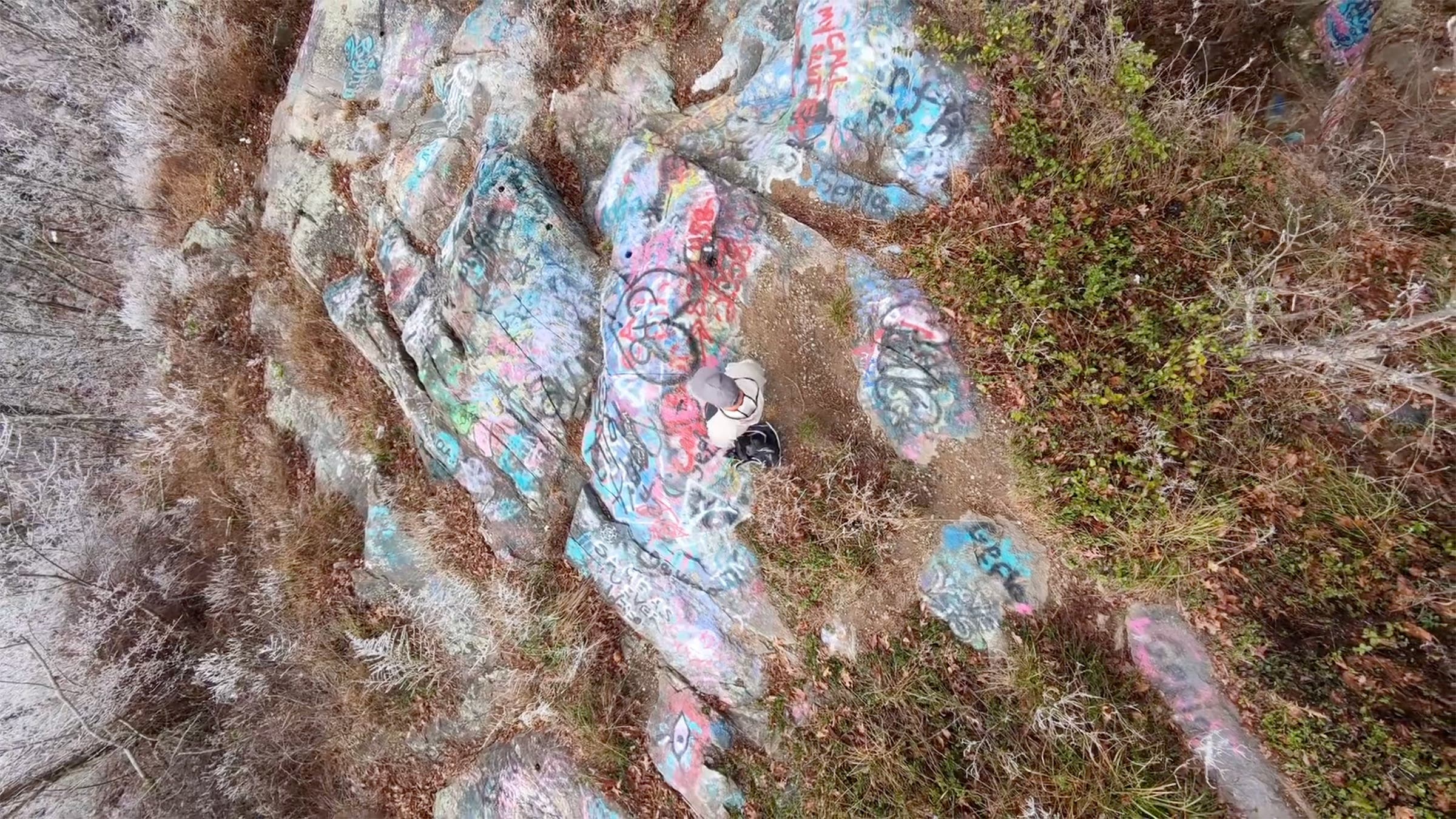 Overhead view of man standing on rock with graffiti, shot with the HoverAir X1 ProMax drone