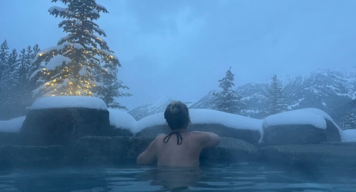 woman with hair in a bun sits in a hot tub facing snow-covered mountains at the One&Only Moonlight Basin