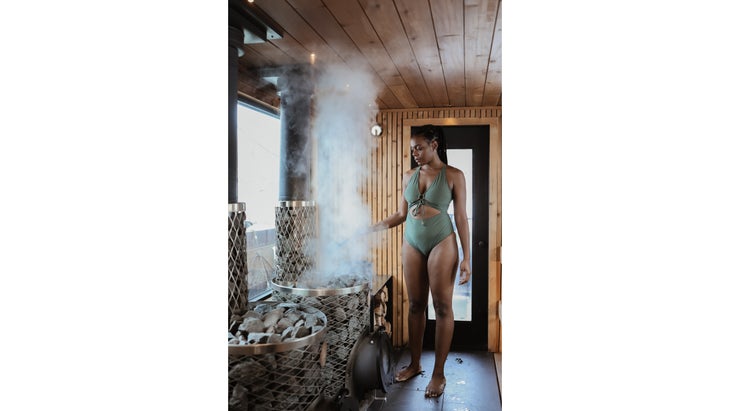 A woman adds water to the hot stones inside a floating sauna.