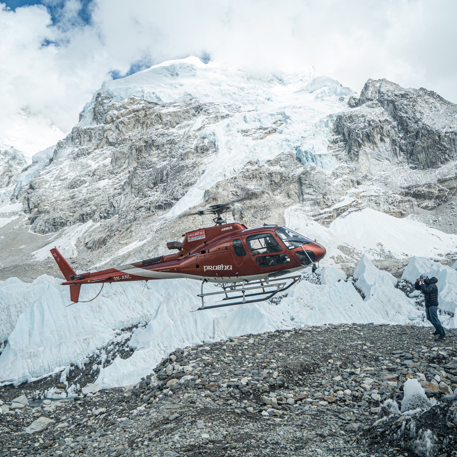A helicopter hovers over a rock clearing with Mount Everest behind.