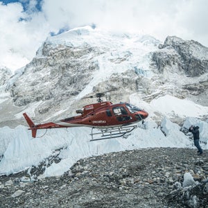 A helicopter hovers over a rock clearing with Mount Everest behind.