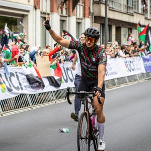 An amputee cyclist raises his hand in a peace sign for the crowd.