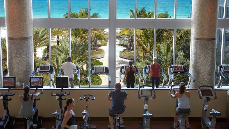 Hotel guests workout on cardio equipment with a beachfront view.