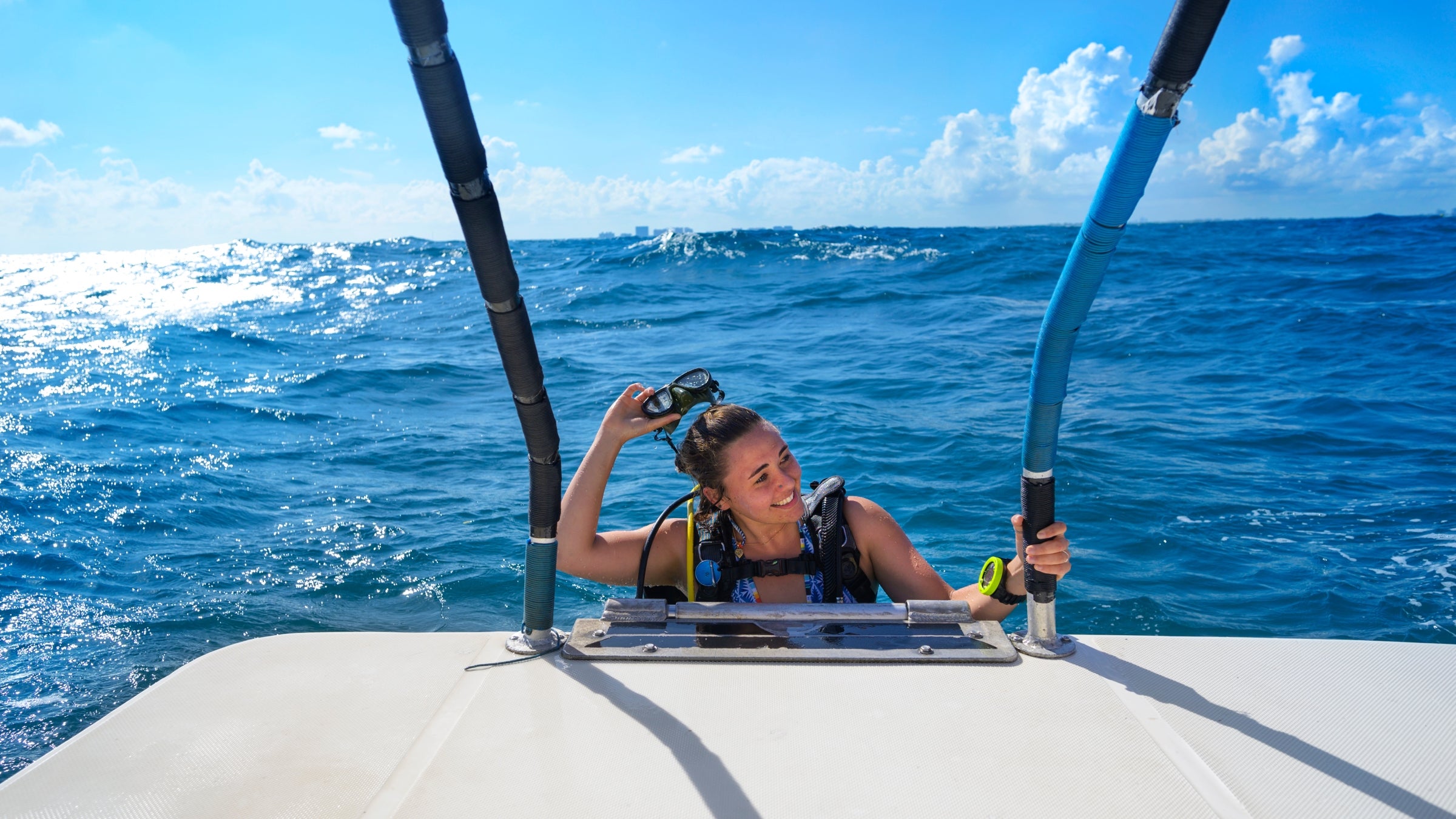 A woman smiles as she takes off her snorkeling mask while climbing aboard a boat.