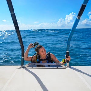 A woman smiles as she takes off her snorkeling mask while climbing aboard a boat.