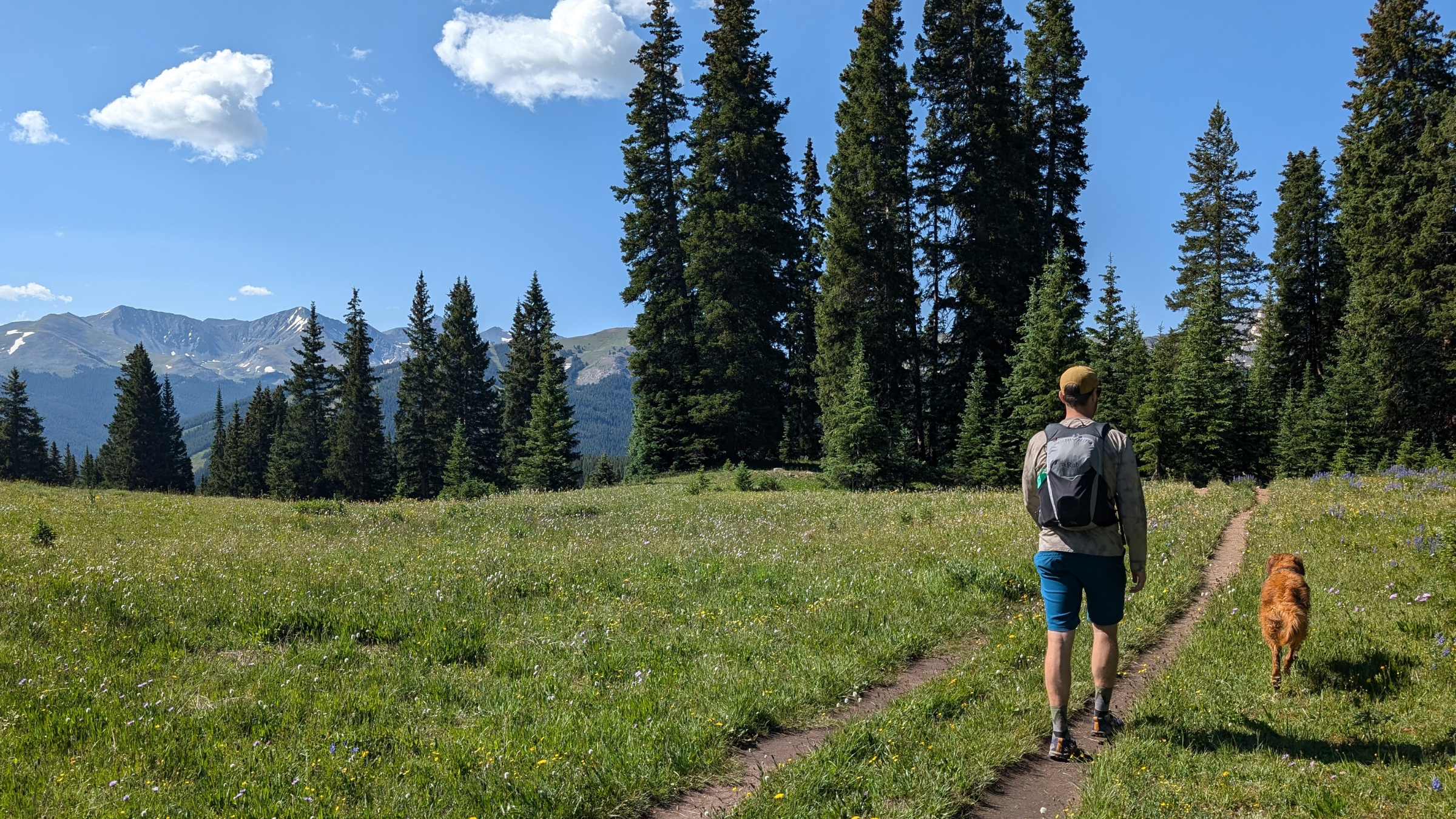 A man hikes with a golden retriever. The man is wearing the Rab Nitron 18 backpack.