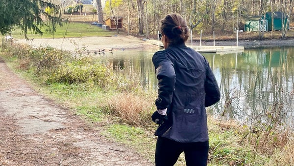 Outside writer Lisa Jhung testing the best winter running jackets for women in 2026, running on a trail next to a pond