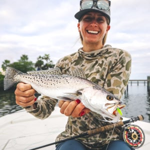 Author Frankie Krempa highlights the essential gear you need for salt water fly fishing. An angler displays a beautiful spotted sea trout caught on a hand-tied fly.