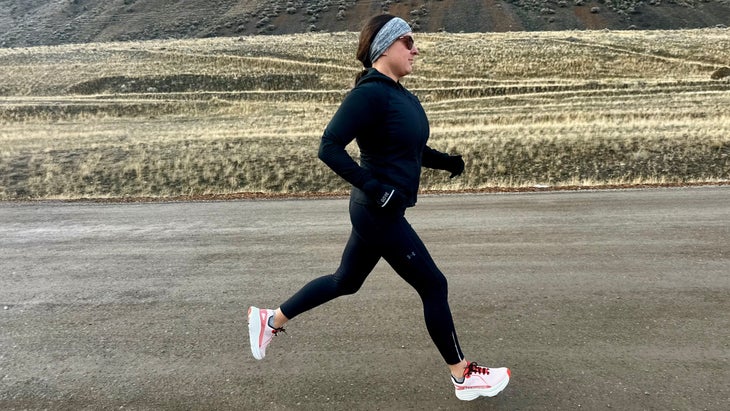 Running shoe tester and author Maggie Slepian strides along a gravel road in open terrain, wearing Nortiv 8 Allswifit ActiveAiry running shoes, with black cold-weather layers and a steady mid-run gait.