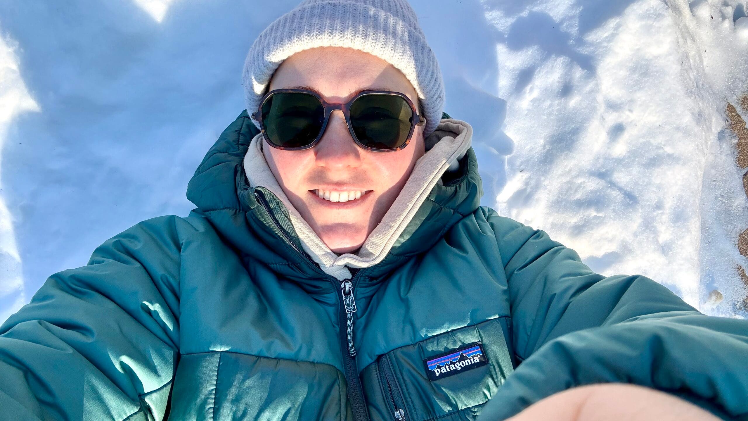 Writer Erica Zazo lies on fresh snow wearing the Ombraz Cammina sun glasses with Patagonia Nano-Air Puff jacket.