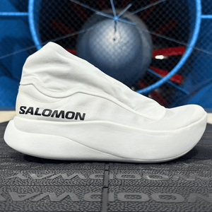 A side profile of the white Salomon S/Lab Phantasm 3 road racing shoe featuring its distinctive aerodynamic lace cover and high-stack PEBA midsole, positioned on a treadmill in a wind tunnel testing environment.