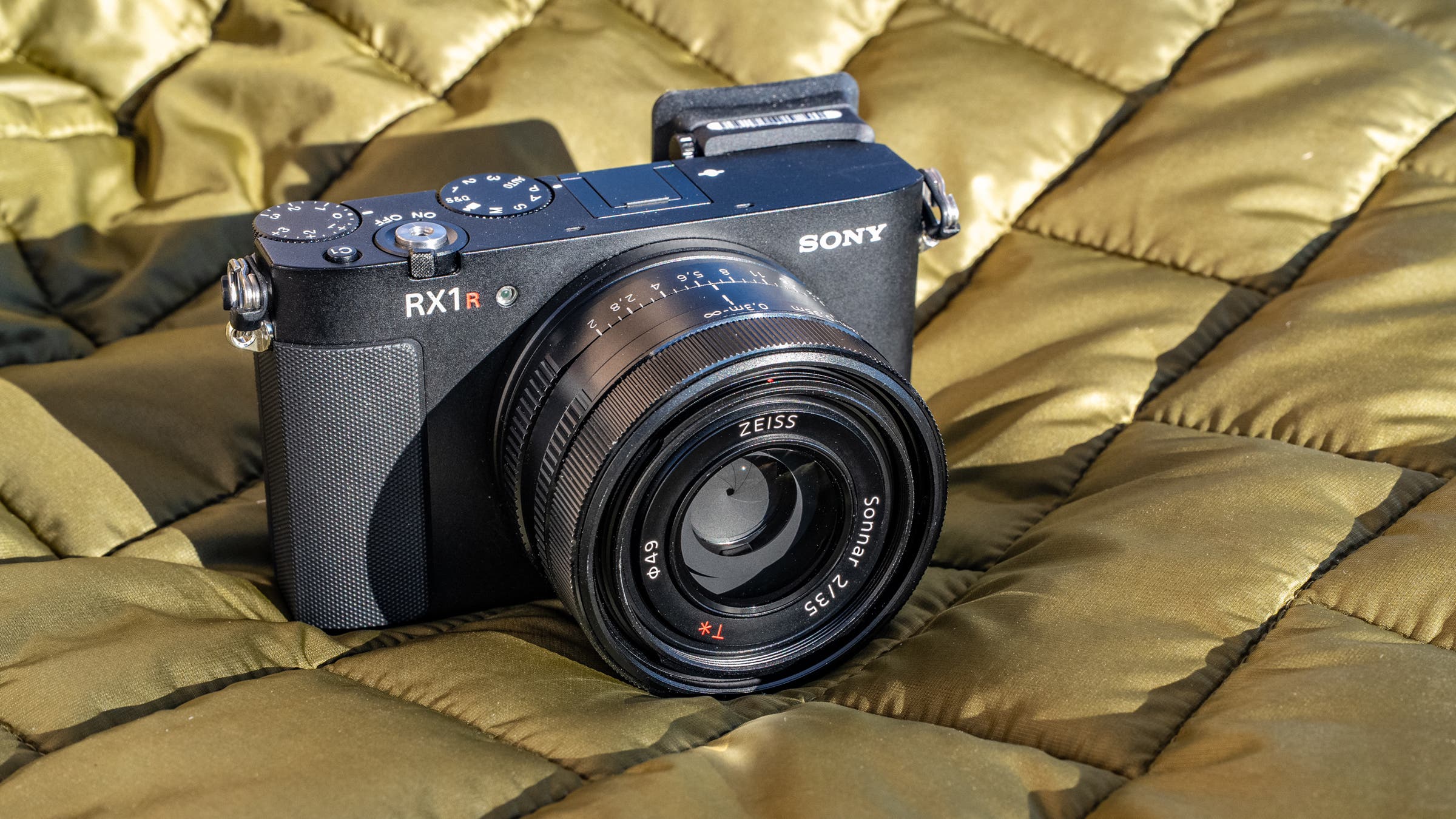 Sony RX1R III pocket camera resting on a quilt outdoors, highlighting its compact body and fixed Zeiss lens; photographed for a story by Jakob Schiller.