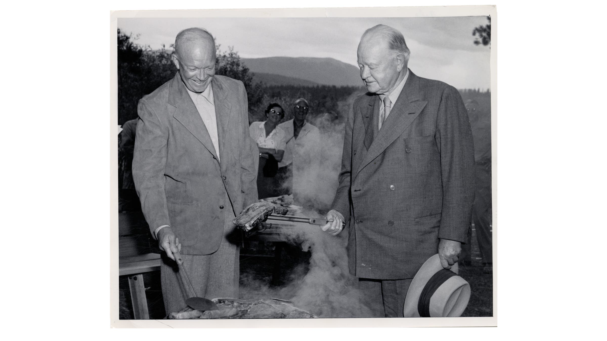 Black and white photo of President Eisenhower cooking a dirty steak while others look on.