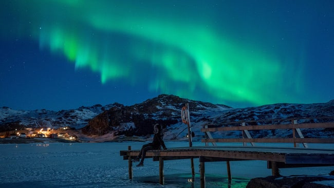 A woman observing northern lights (Aurora borealis), on the Lofoten Islands, in Bostad, in the arctic circle in northern Norway.