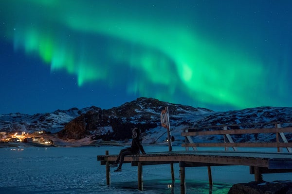 A woman observing northern lights (Aurora borealis), on the Lofoten Islands, in Bostad, in the arctic circle in northern Norway.