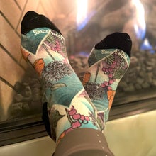 A close-up of colorful, botanical-patterned Smartwool socks being warmed in front of a glowing indoor fireplace.