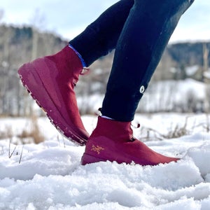 A runner steps through fresh snow wearing burgundy Arc’Teryx Nivalis winter running shoes with grippy soles and insulated uppers, paired with black tights, in a cold, wintry landscape; photo by Lisa Jhung.