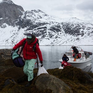 Man in red jacket carrying duffel bag over rocks in Greenland