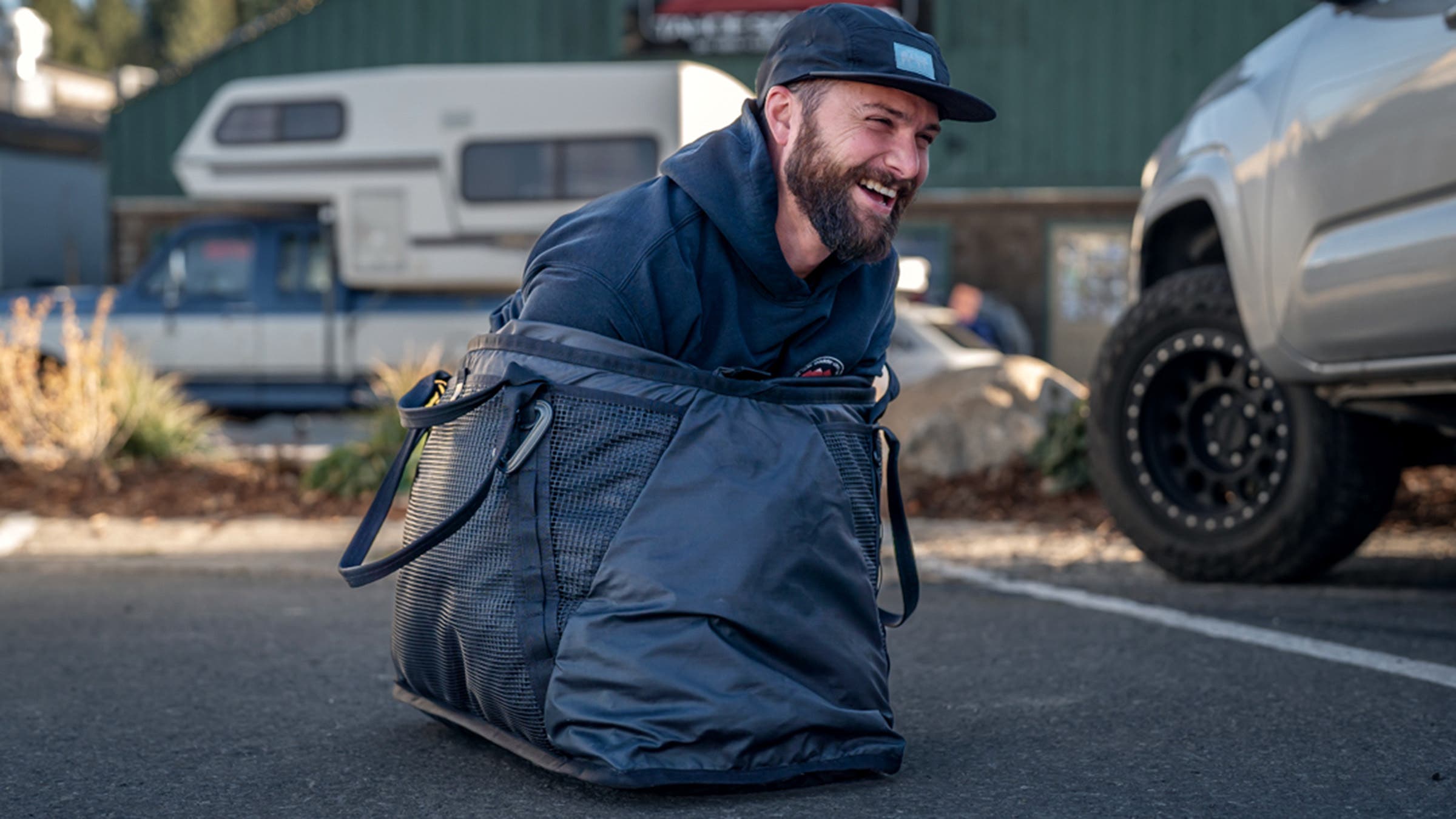 Man squeezing himself inside a duffel bag in parking lot