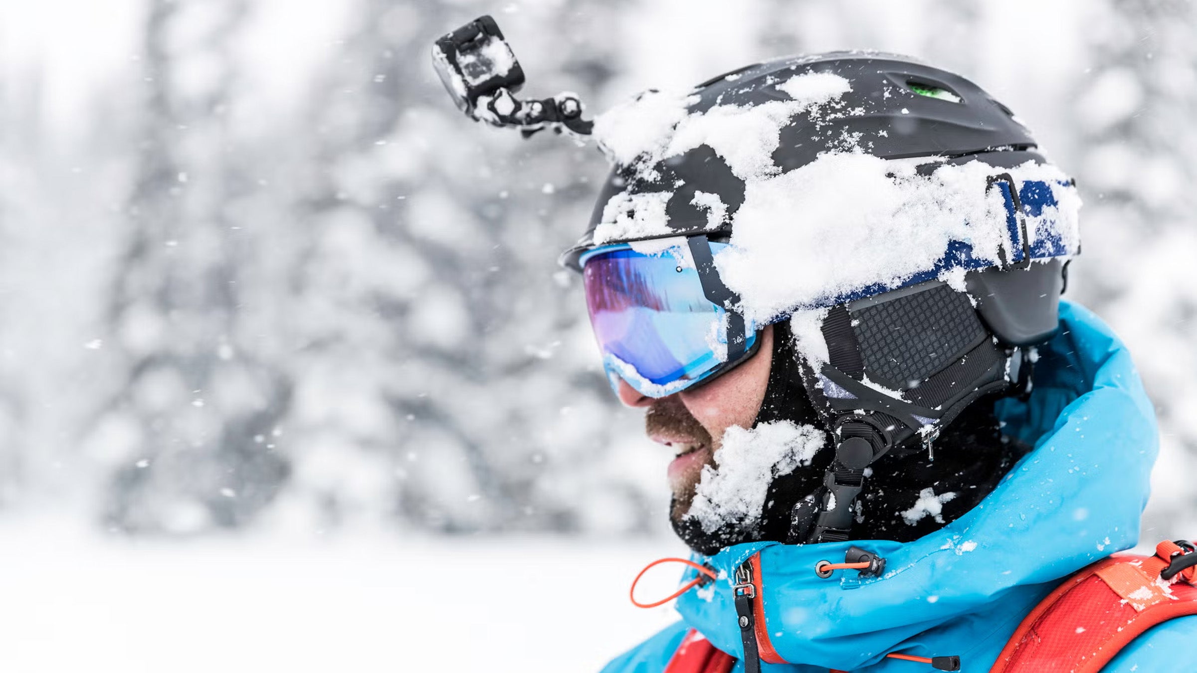 Closeup headshot of skier wearing black GoPro helmet camera in front of snowy background