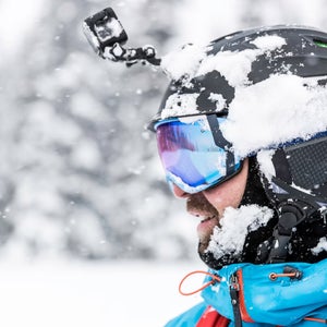 Closeup headshot of skier wearing black GoPro helmet camera in front of snowy background
