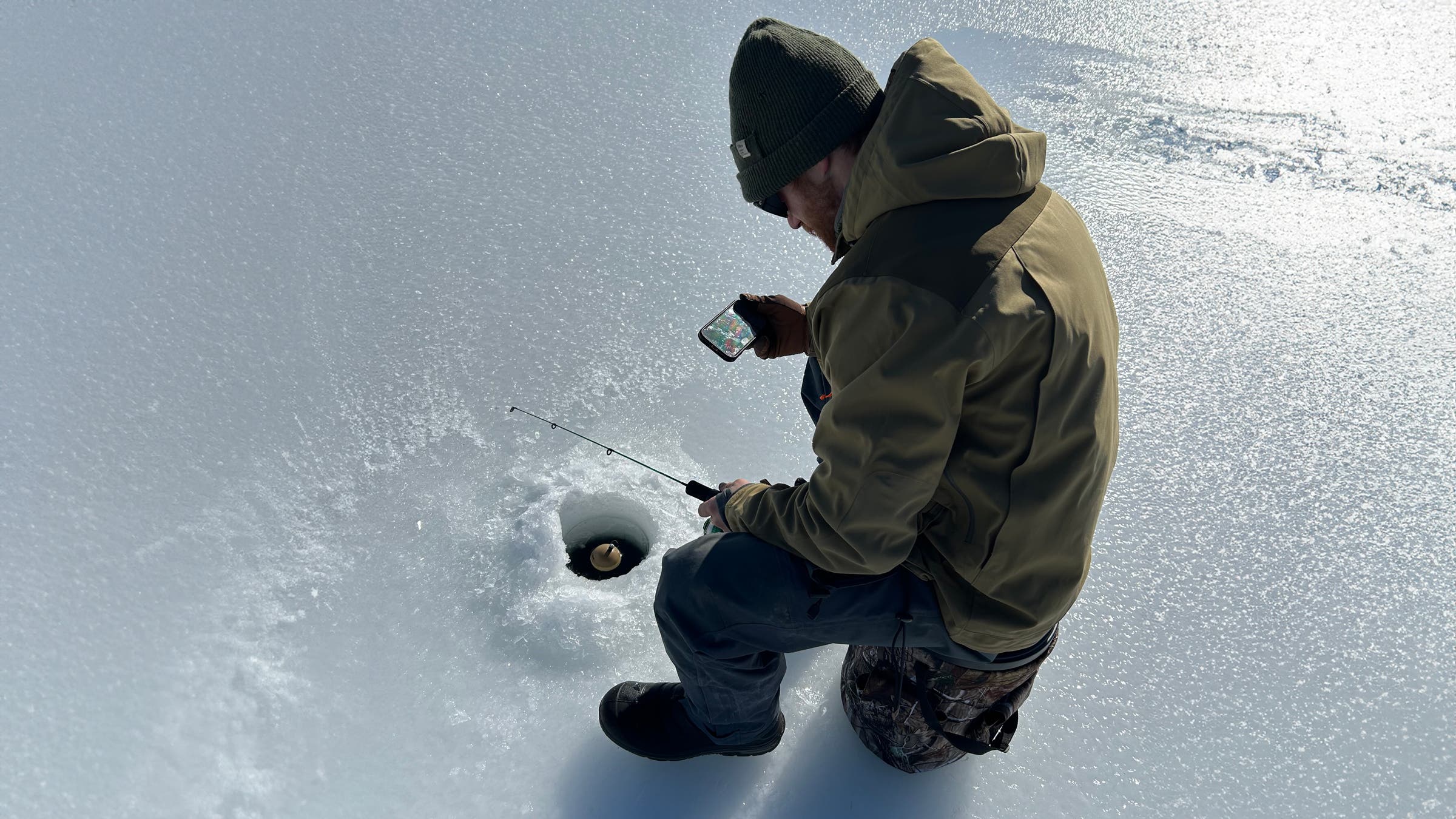 A Deeper PRO+ 2 Portable Fish Finder floating in a freshly drilled ice hole, showing compact, high-tech ice fishing gear used to scan depth and locate fish beneath the frozen surface.