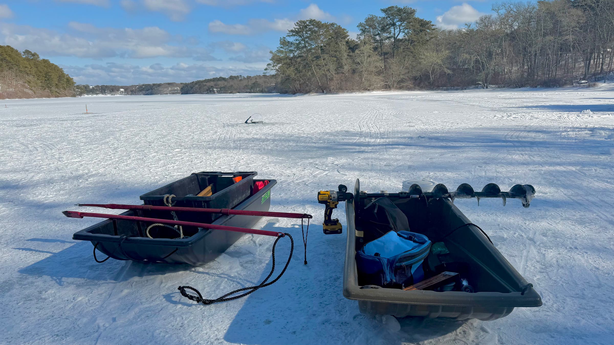 Two Pelican Multi-Purpose Utility Sled units sit on a frozen lake loaded with augers, a power drill, rods, and tools, neatly organizing essential ice fishing gear for drilling holes and moving between spots on the ice.