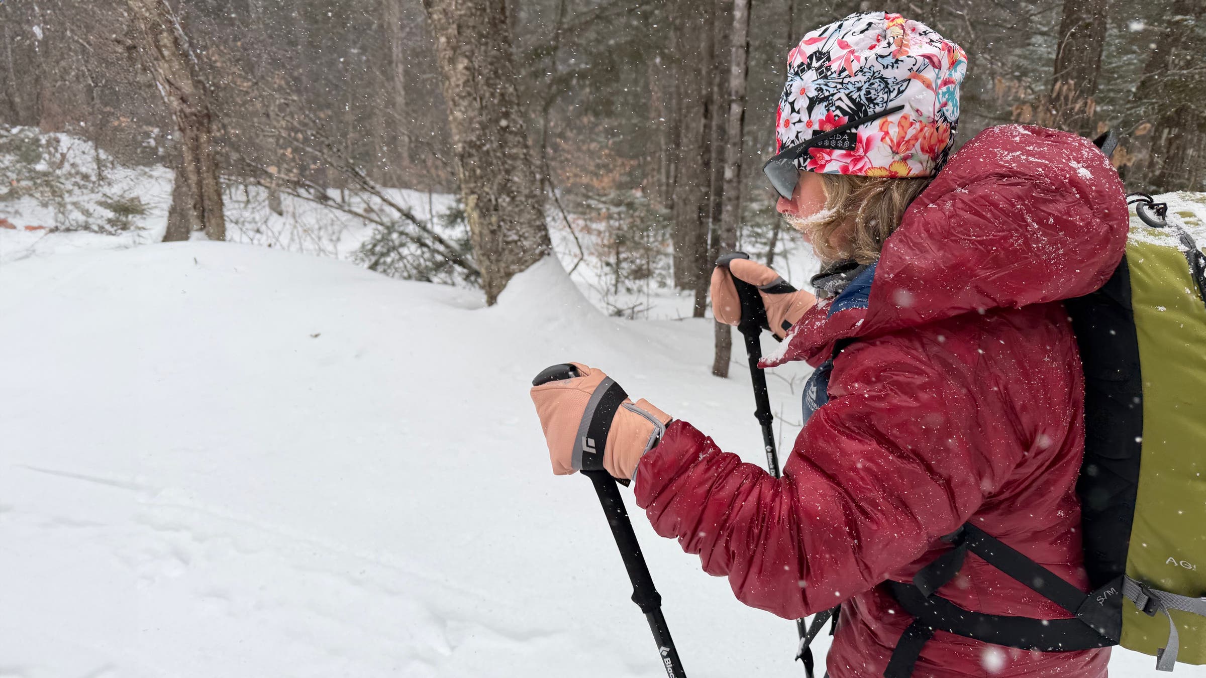 A winter skier travels along a snow-covered forest trail in the Mountain Equipment Oreus Hooded Jacket, a durable synthetic jacket built for warmth and performance in cold, active conditions.