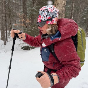 A winter cross-country skier moves through a snowy forest trail wearing the Mountain Equipment Oreus Hooded Jacket, a warm, weather-resistant synthetic jacket designed for active cold-weather adventures.